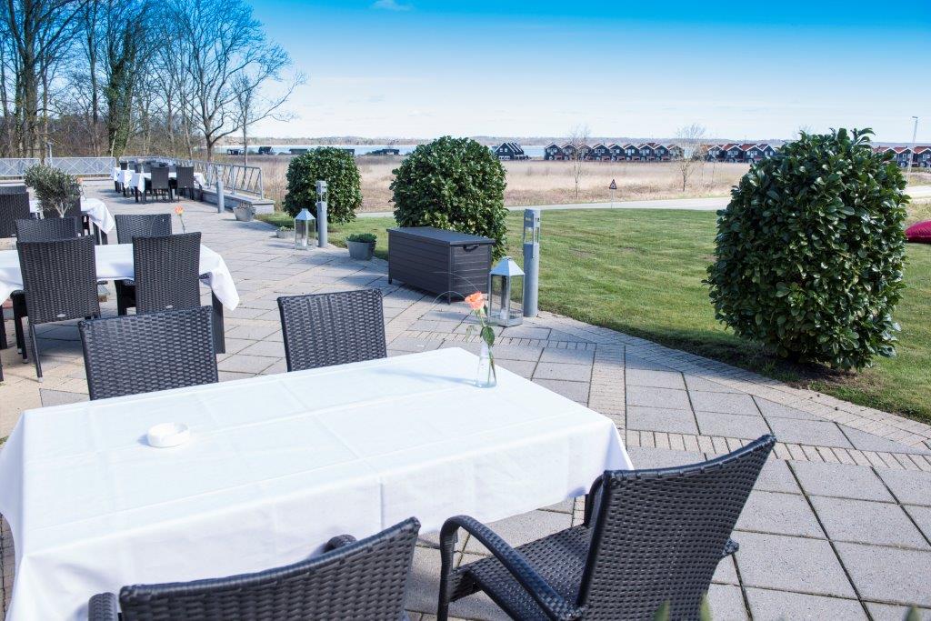 Udendørs terrasse med bord med hvid dug og stole ved Hotel Juelsminde Strand i Destination Kystlandet