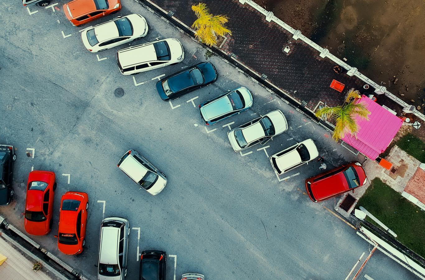 Parkeringsplads set ovenfra med parkerede og kørende biler