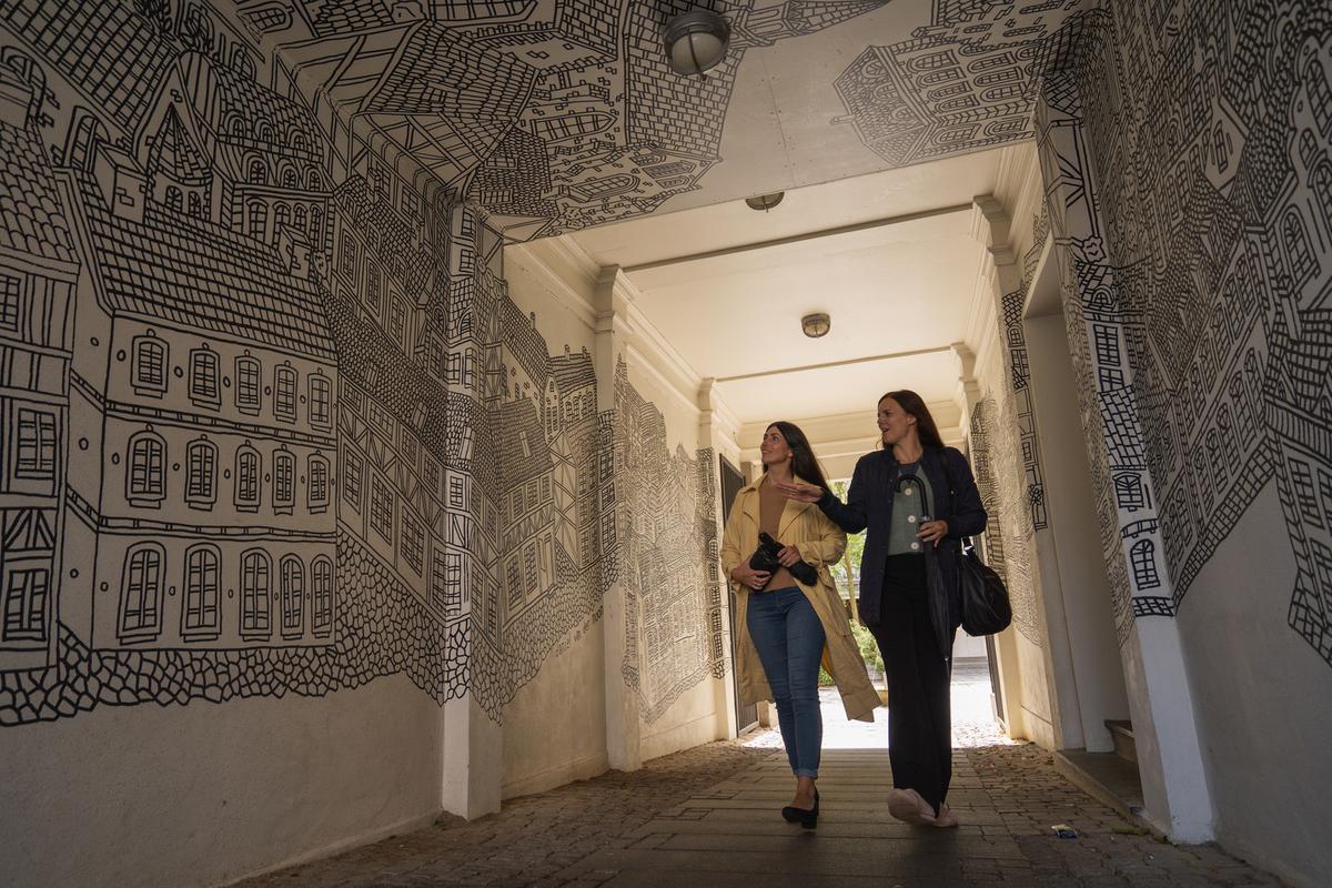 To voksne kvinder i regnvejr ser street art af Daniel Van der Noon i  Destination Kystlandet. 