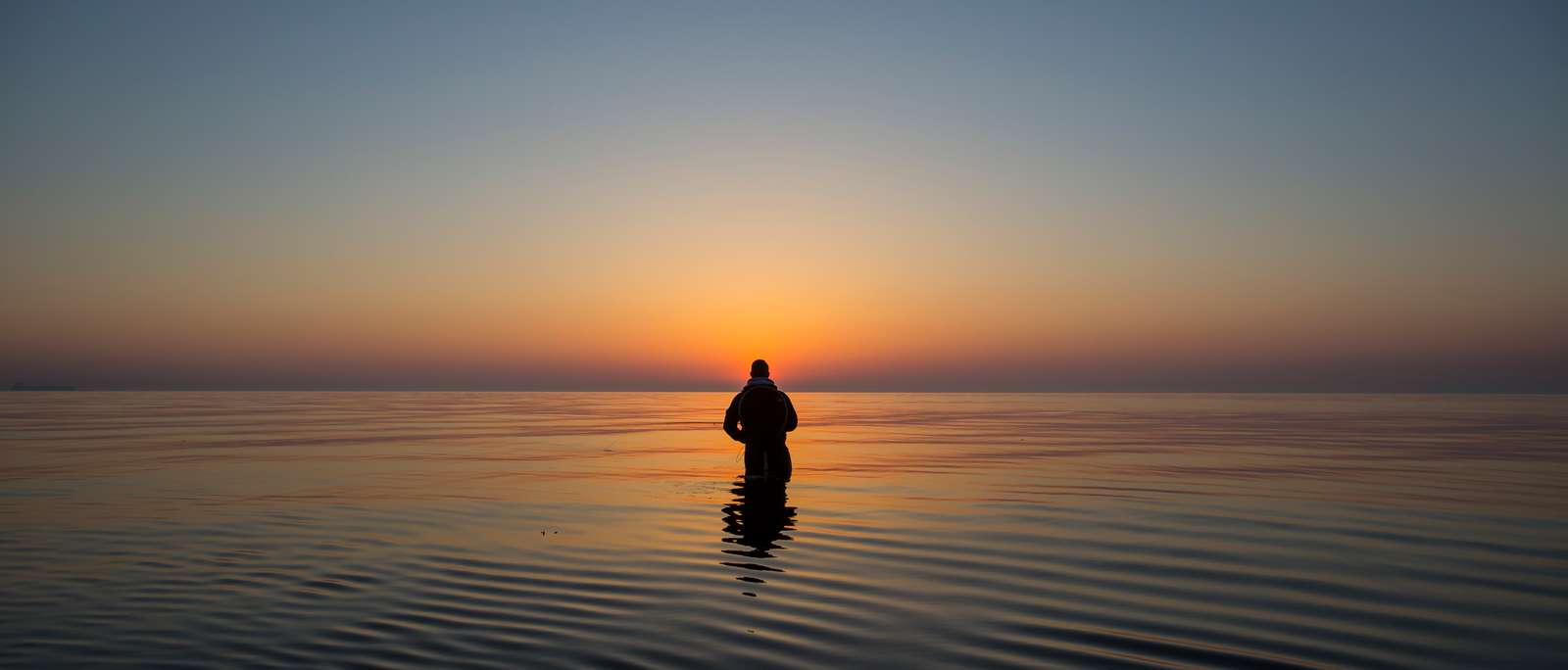 Mand fisker i havet ved solopgang