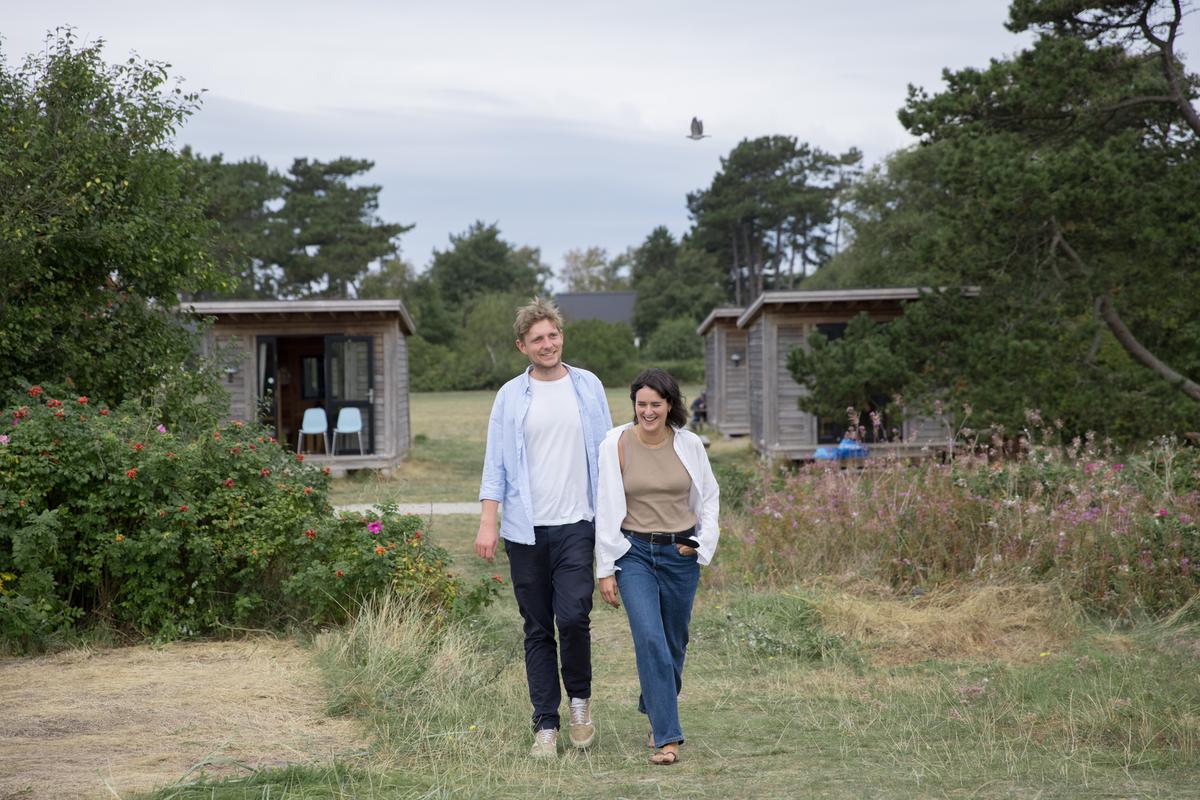 En mand og en kvinde går ved Tunø Strand ved hytter i Destination Kystlandet