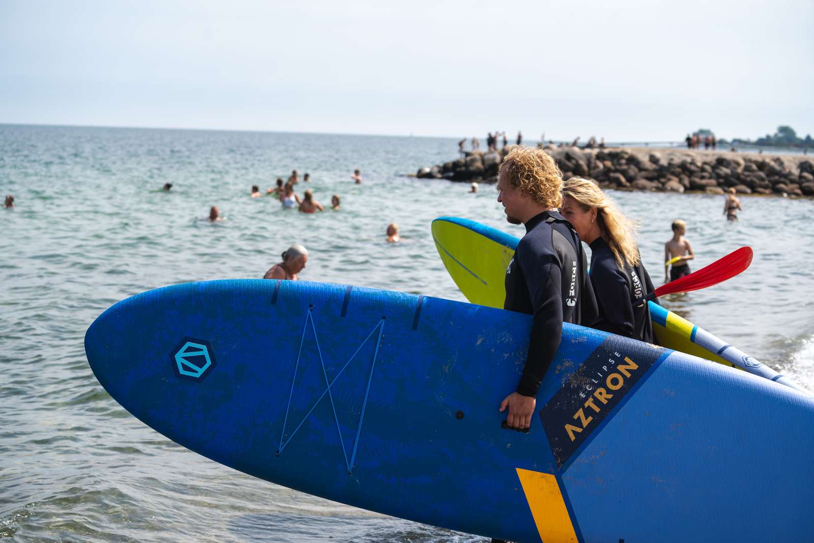 Et par har SUP boards under armen og går ud i vandet på Storstranden i Juelsminde