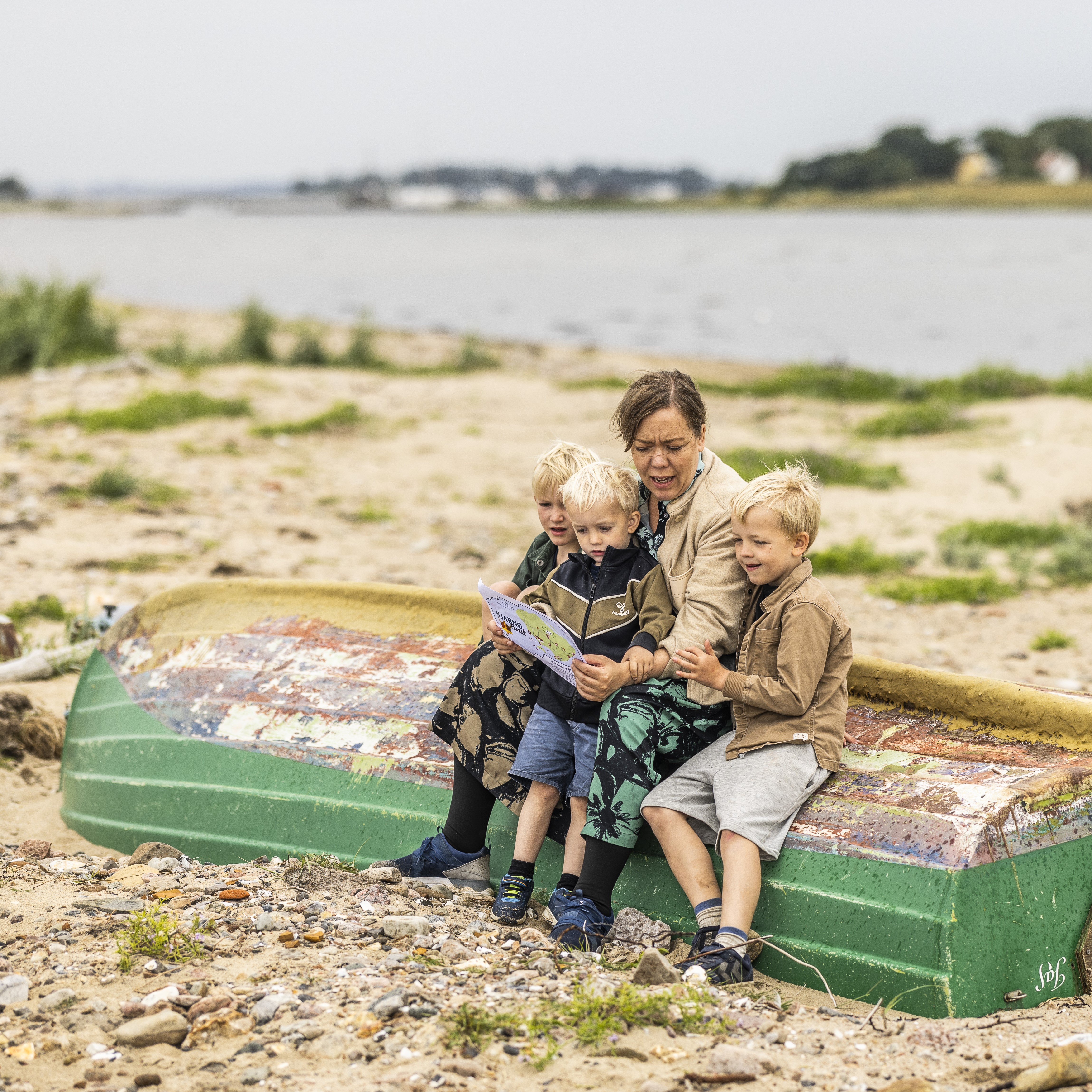 En kvinde sidder med tre små drenge på en strand med et skattekort