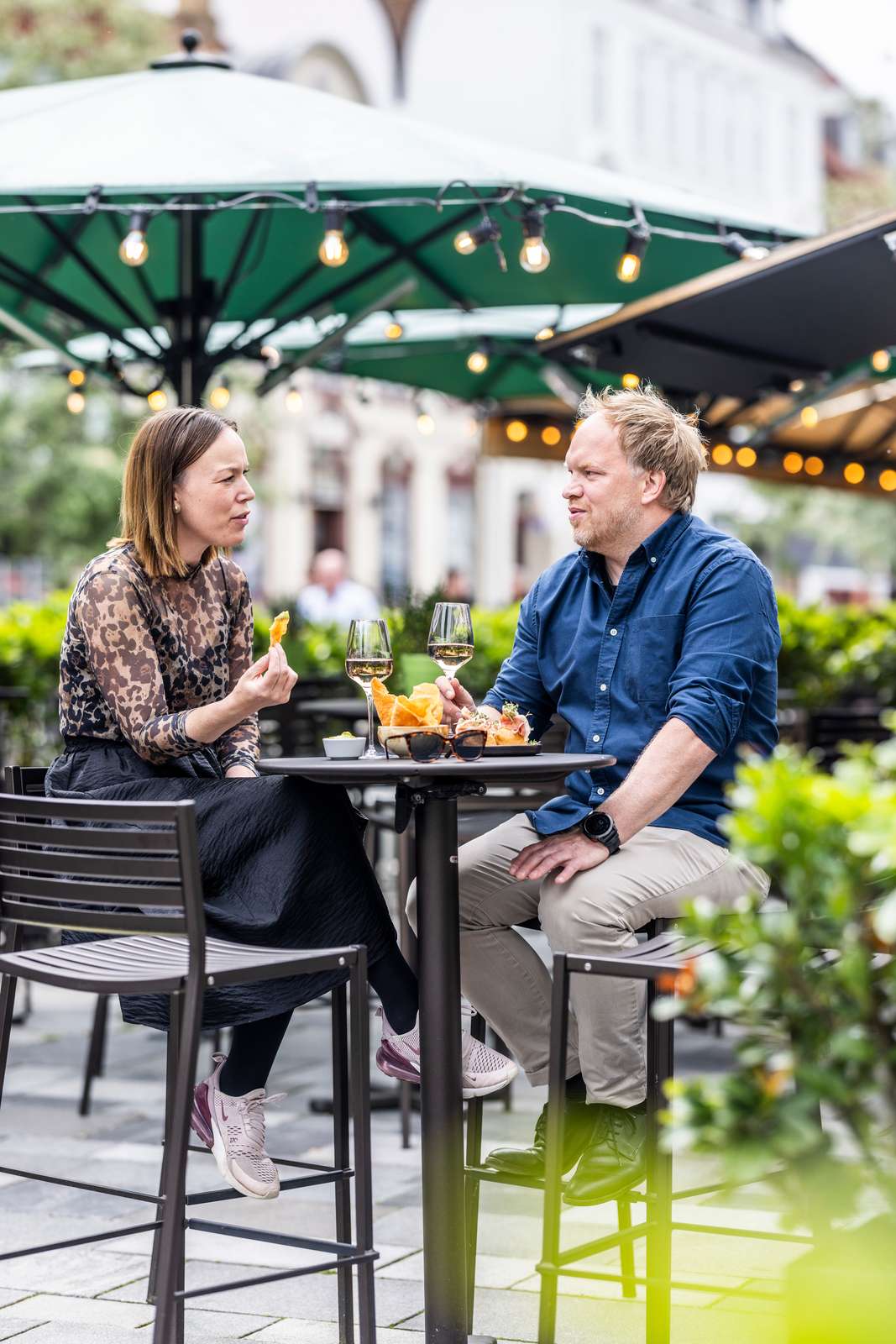 A man and a woman are sitting outside at a bar table under a green parasol