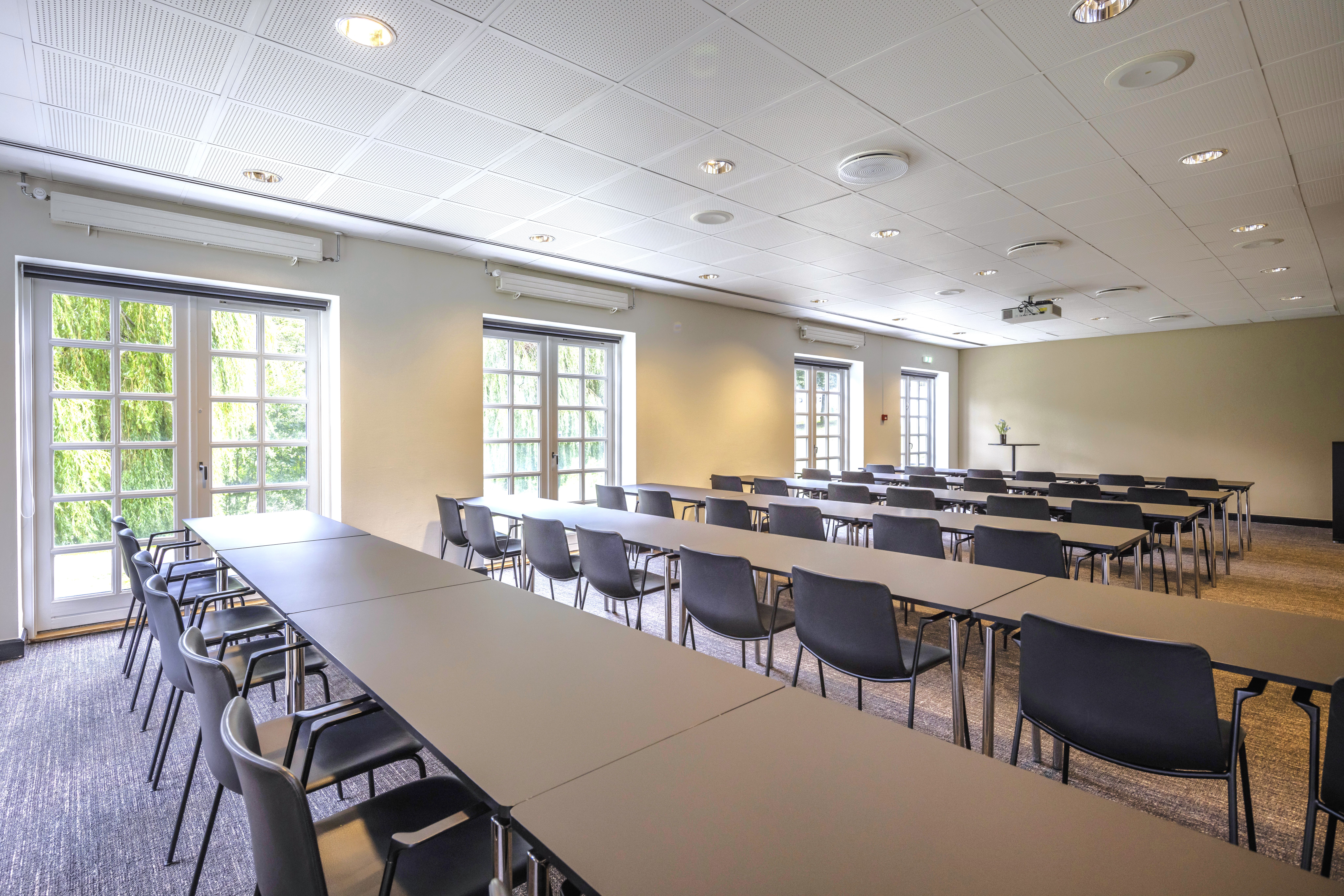 Mødelokale med hvide borde, sorte skalstole og franske vinduer ud til en grøn park