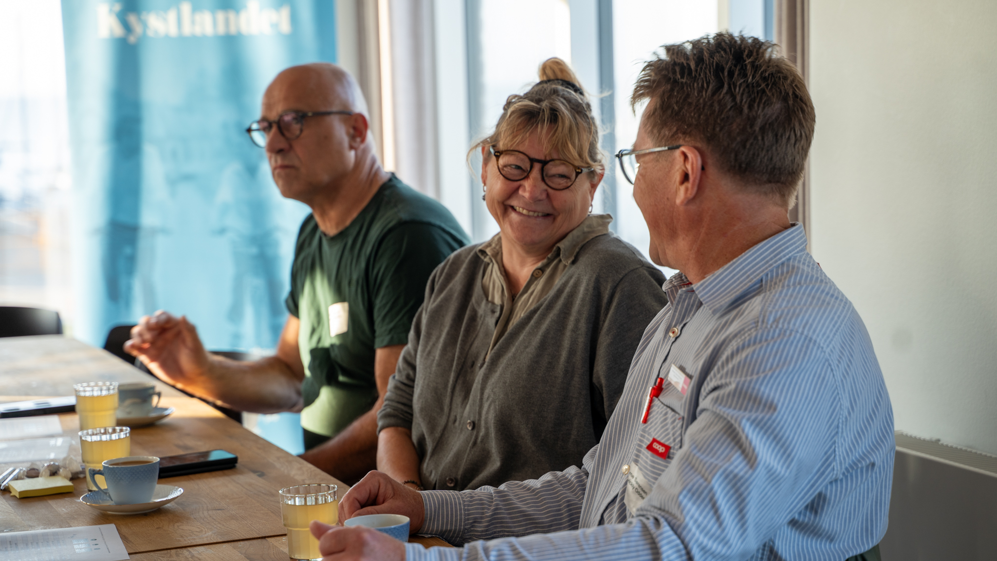 tre mennesker sidder på række ved et mødebord