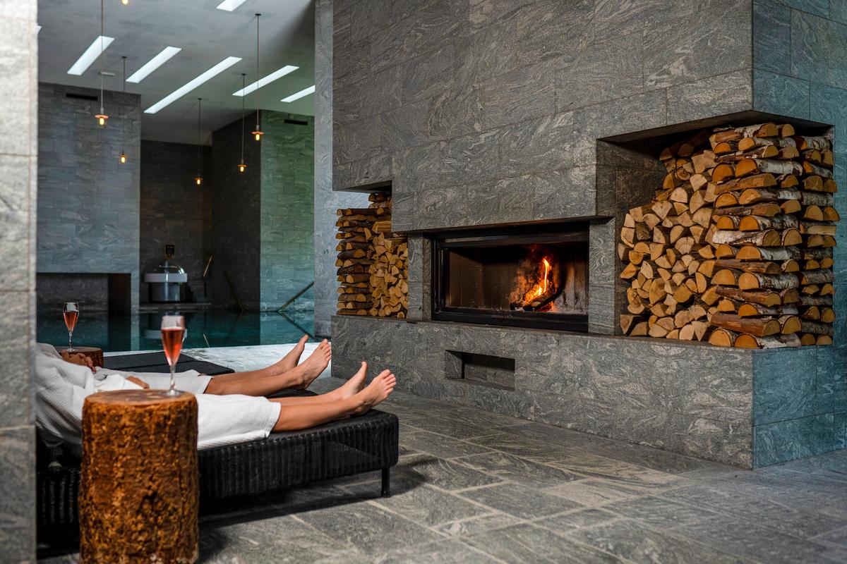 Et par sidder i liggestole foran pejsen i spaen hos Hotel Vejlefjord