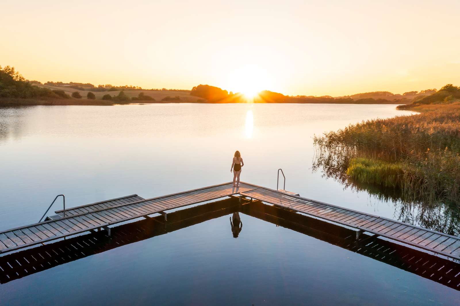 Kvinde kigger på solnedgang fra badebroen ved Ring Sø