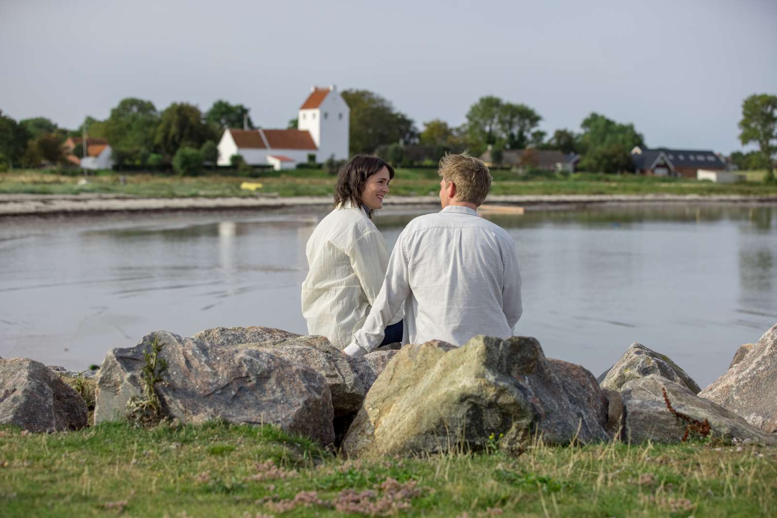 Et par sidder på en sten ved vandet med Endelave Kirke i baggrunden