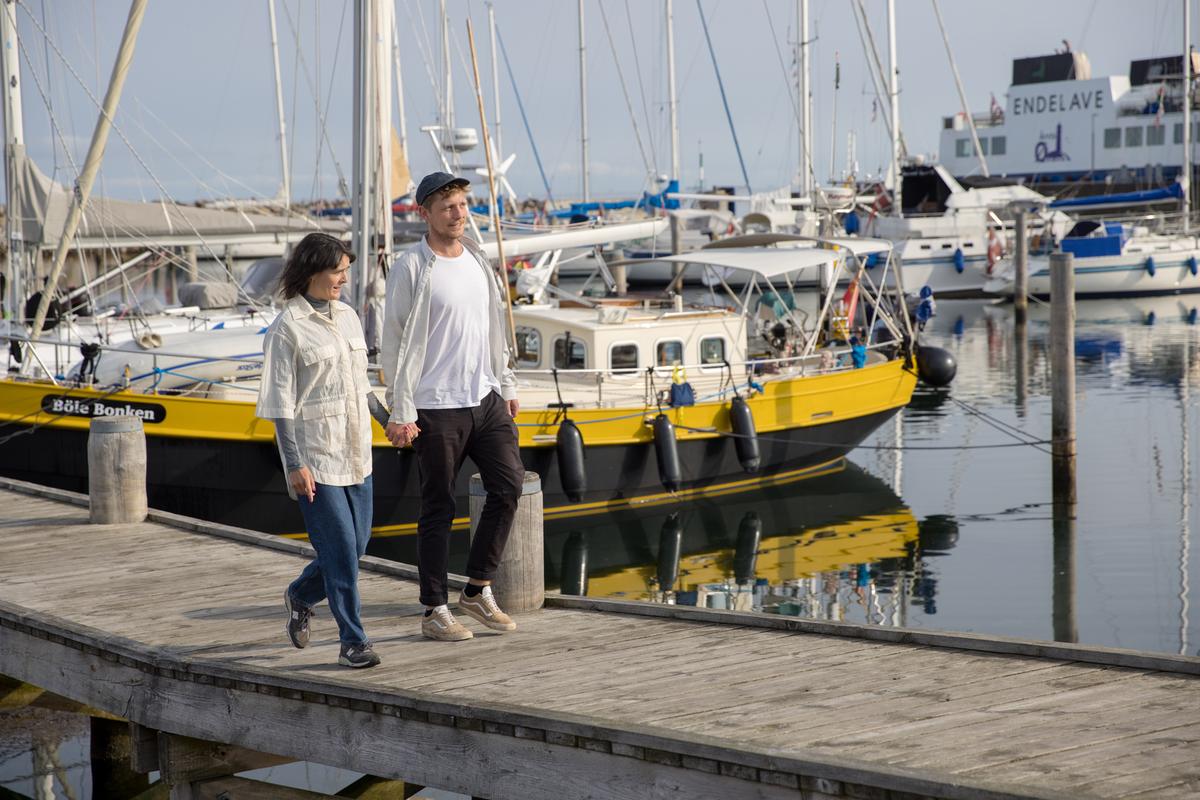Par går ved marinaen på Endelave med Endelavefærgen i baggrunden