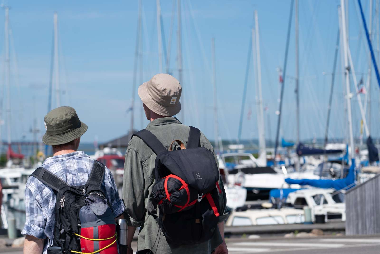 To mænd med rygsæk og bøllehat går ved lystbådehavnen i Snaptun
