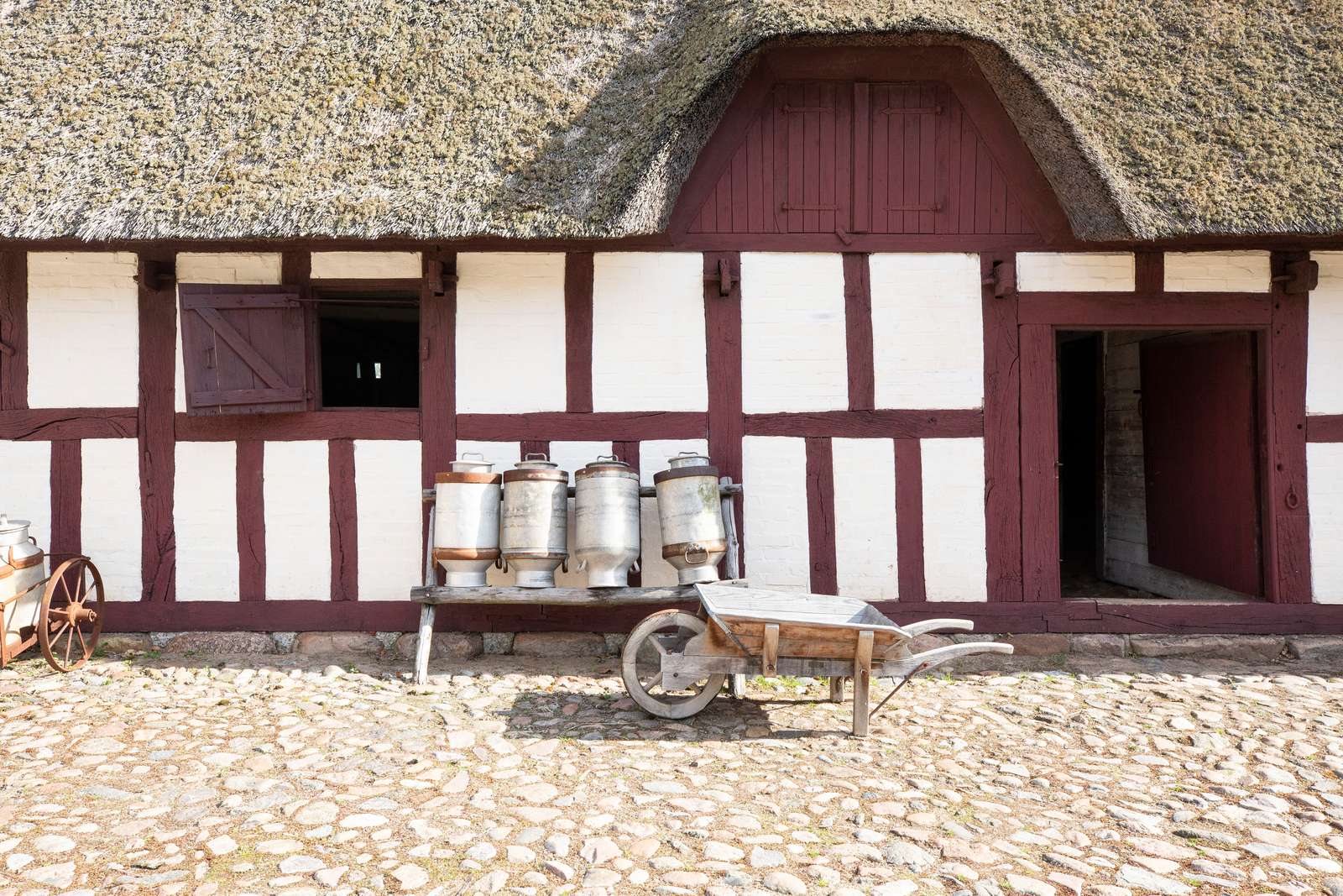 Mælkejunger på gårdsplads foran facade på stråtækt bindingsværkshus på Glud Museum
