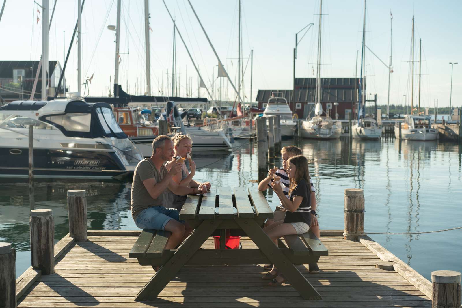 Familie sidder ved borde/bænkesæt på Juelsminde Havn og spiser isvafler