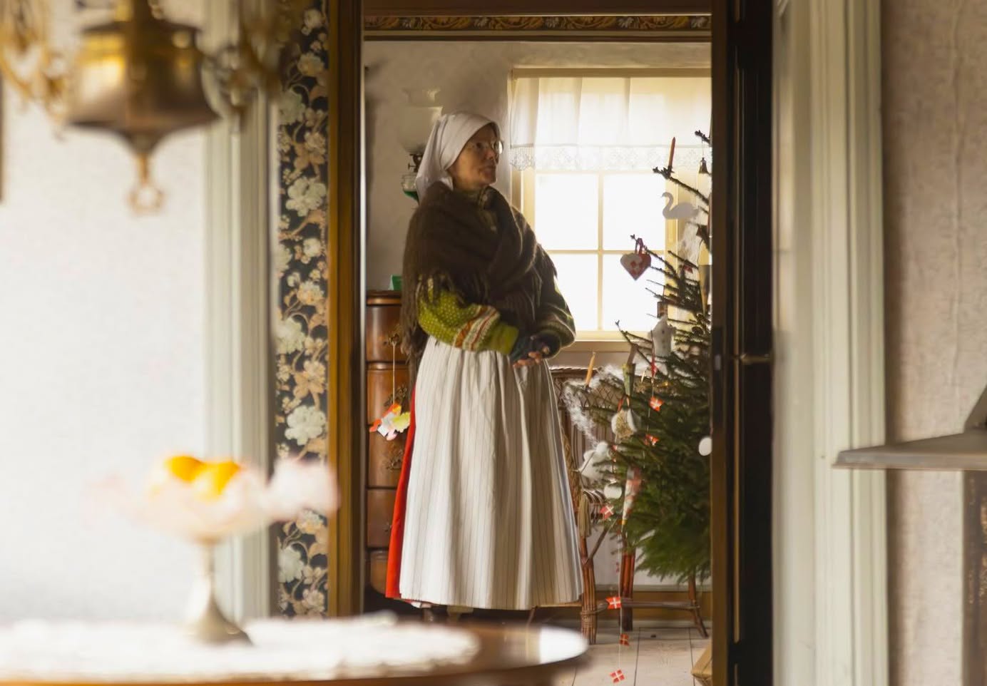 En julepyntet kvinde foran et juletræ i Badensminde på Glud Museum