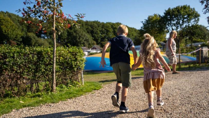 Two children with holding hands at full speed on their way to the bouncy castle in the playground at Horsens City Camping - part of Destination Coastal Land