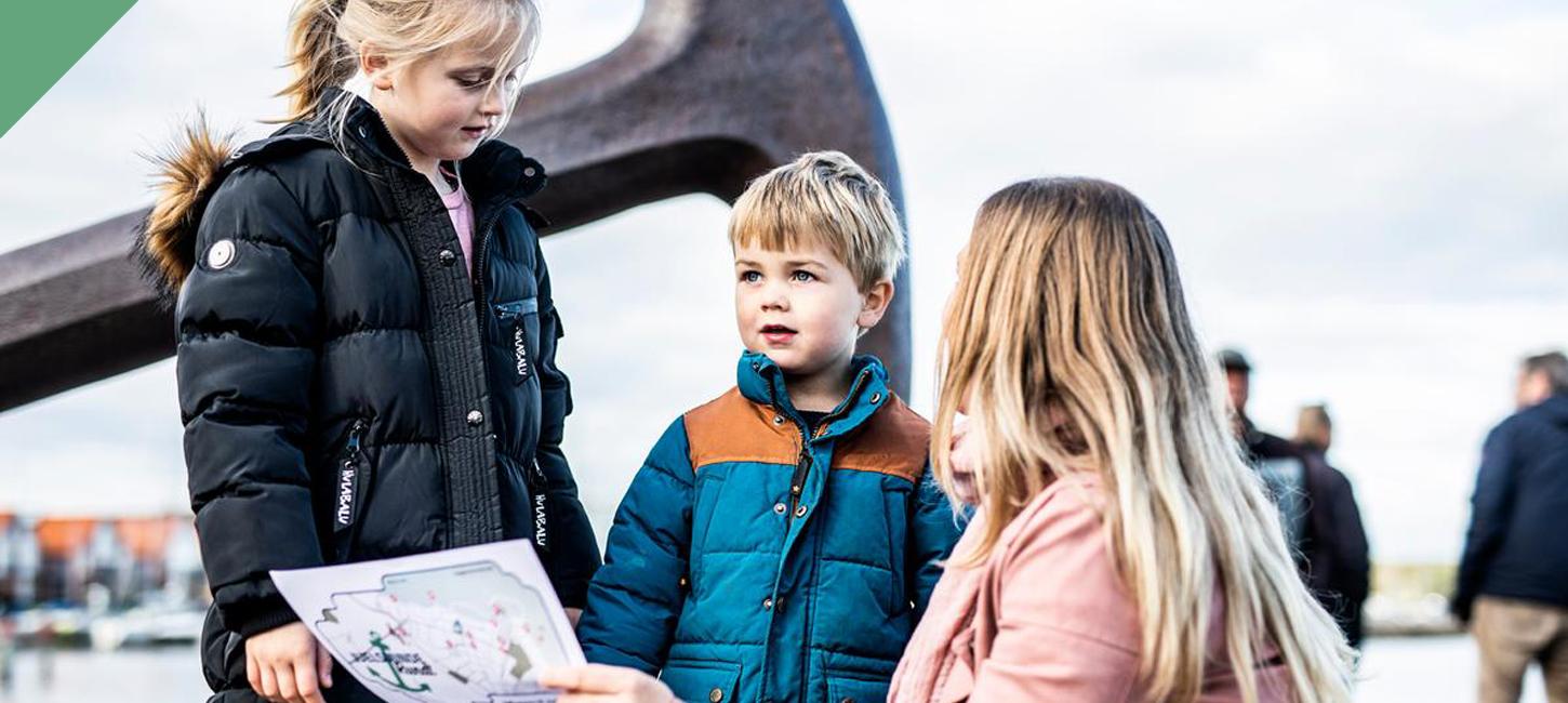 Mother and two children looking at treasure maps in front of the anchor in Juelsminde