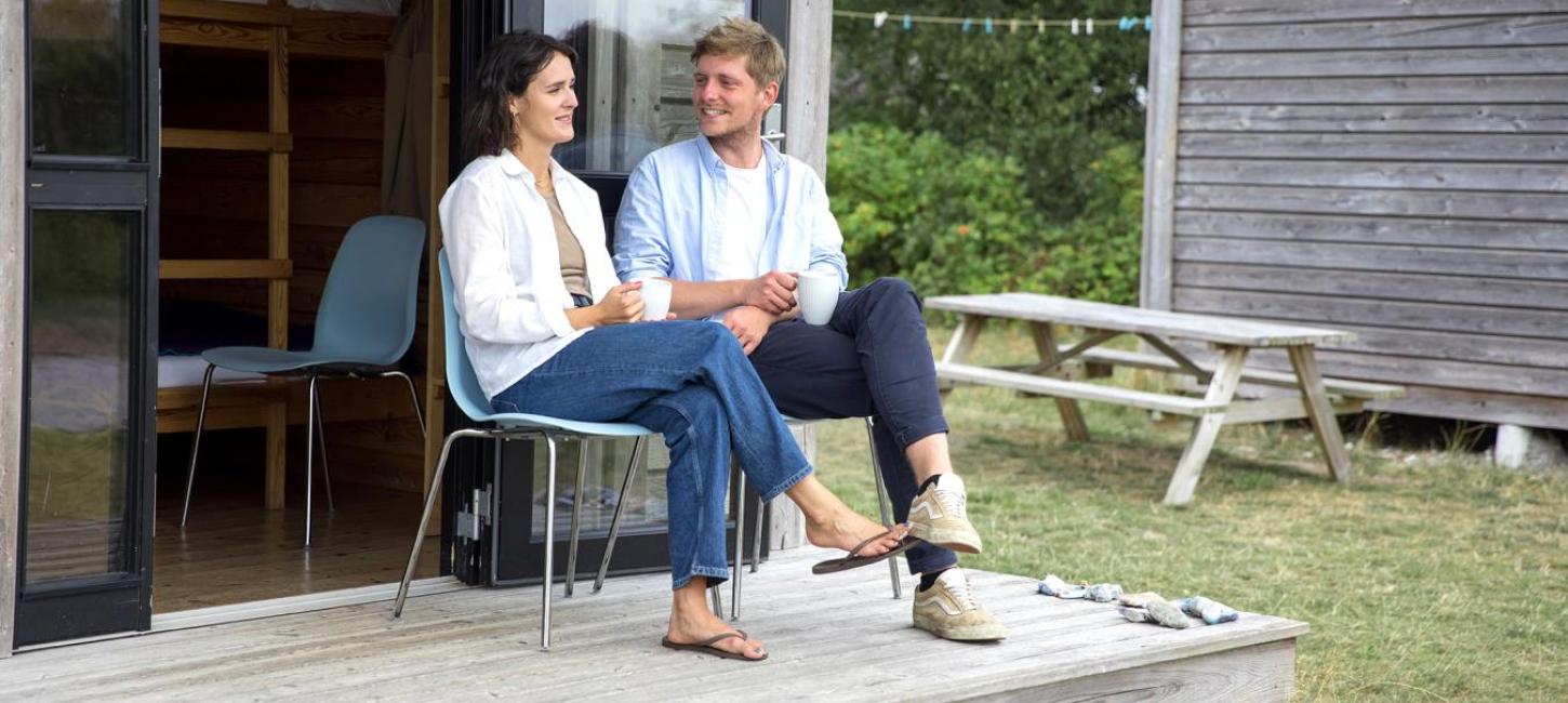 Couple sitting and talking in front of a cottage at Tunø Tent Site in Destination Coastal Land