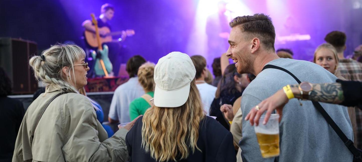 A man and two women in a festival atmosphere and concert in front of a large stage at music venue Platform K in Horsens.