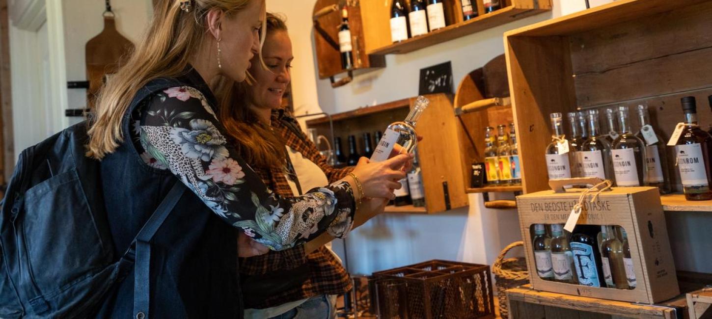 Two women looking at delicacies and spirits at Alrø Købmandsgaard in Destination Coastal Land