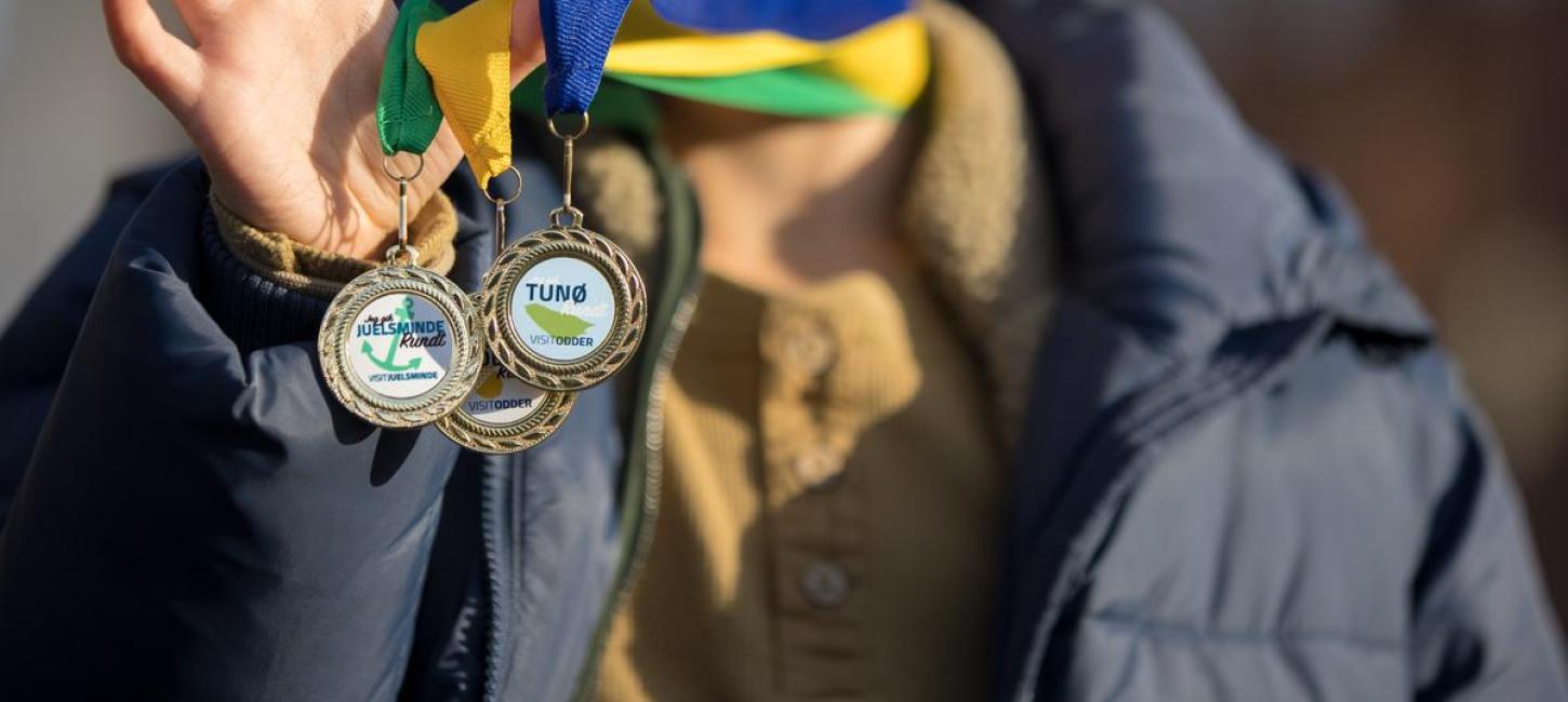 Boy smiles as he holds three medals from the free scavenger hunts in the Coastal Land in Denmark
