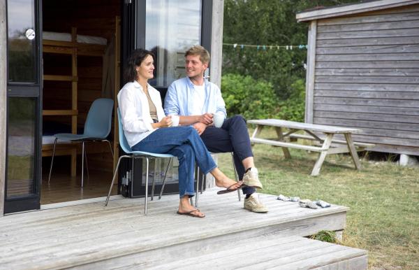 Couple sitting and talking in front of a cottage at Tunø Tent Site in Destination Coastal Land