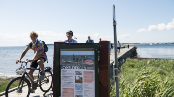 Cyclists on Alrø with a sign for the bicycle ferry in the foreground