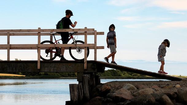Far med to børn nyder udsigten på cykeltur ved bro hen over vand