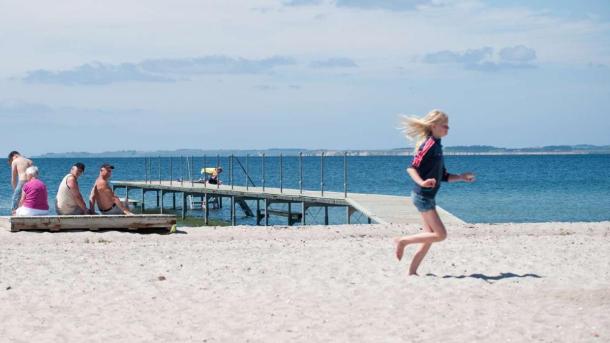 Girl running along Hou Beach at Hou Strand Camping while the grandparents watch in the background