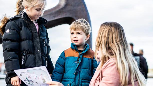 Mother and two children looking at treasure maps in front of the anchor in Juelsminde