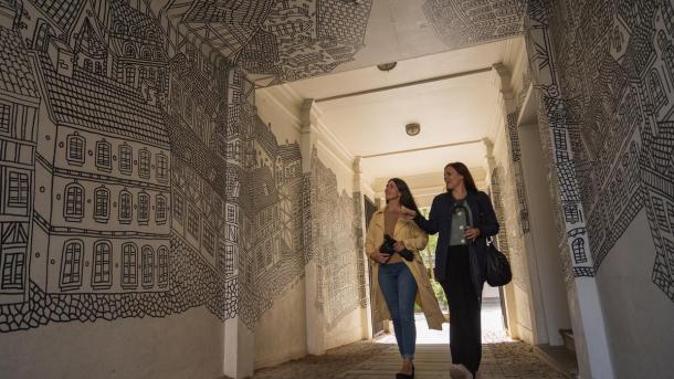 To voksne kvinder i regnvejr ser street art af Daniel Van der Noon i  Destination Kystlandet. 