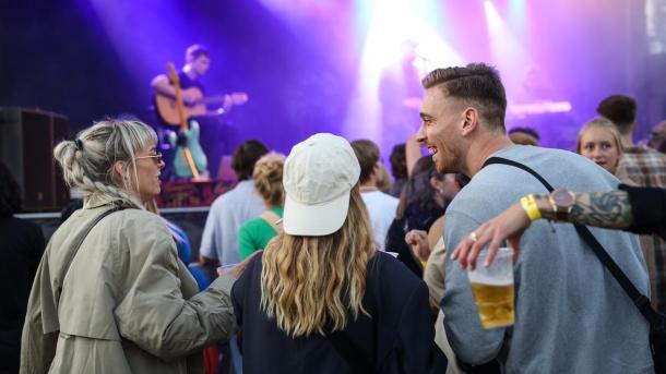 A man and two women in a festival atmosphere and concert in front of a large stage at music venue Platform K in Horsens.