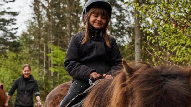 Pige ridder på brun hest med en guide 