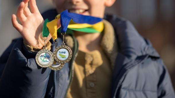 Boy smiles as he holds three medals from the free scavenger hunts in the Coastal Land in Denmark
