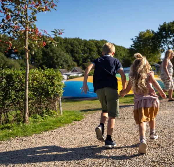 Two children with holding hands at full speed on their way to the bouncy castle in the playground at Horsens City Camping - part of Destination Coastal Land