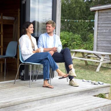 Couple sitting and talking in front of a cottage at Tunø Tent Site in Destination Coastal Land