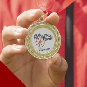 Child in a red top shows a medal for the Horsens Rundt treasure hunt - one of four treasure hunts in Destination Coastal Land