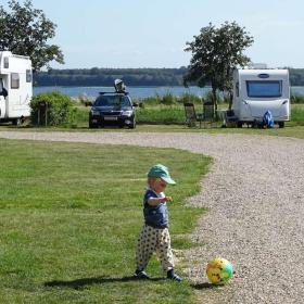 Little boy playing with a ball on the lawn at Horsens City Camping with mobile homes and Horsens Fjord in the background