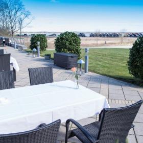 Outdoor terrace with a table with white tablecloth and chairs at Hotel Juelsminde Strand in Destination Coastal Land