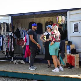 A group of young people standing by a blue shipping container filled with clothes on rails at Platform K cultural centre in Horsens in Destination Coastal Land