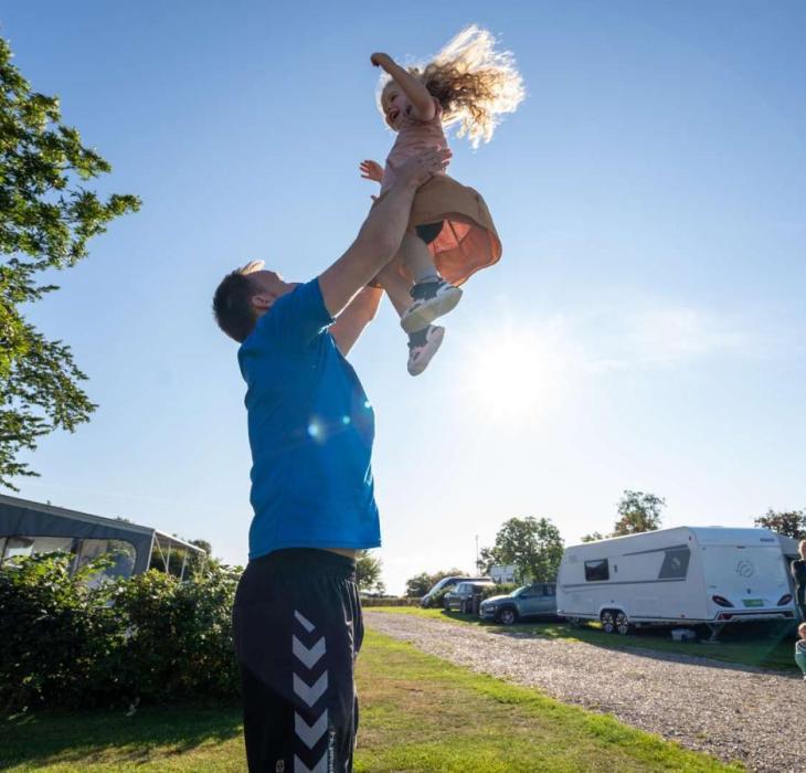 Dad playing with his daughter and throws her into the air in front of a caravan at Horsens City Camping - part of Destination Coastal Land